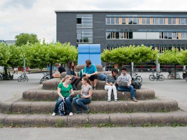 seven students sitting outside a university building in summer